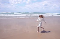 a woman in a white dress running on a beach